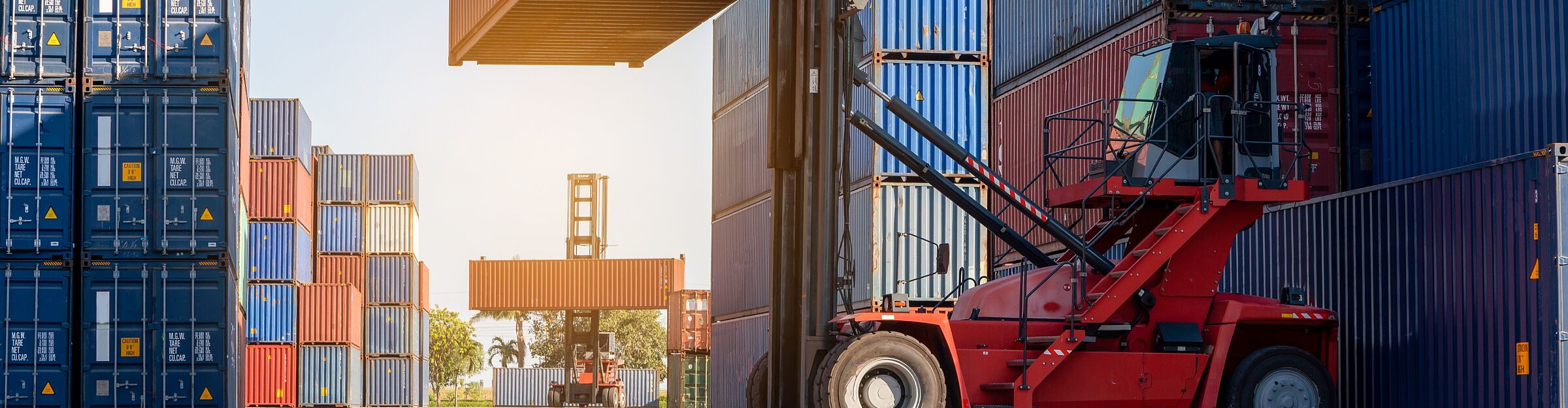 Containerstapler hebt Frachtcontainer zwischen gestapelten Überseecontainern im Depot.