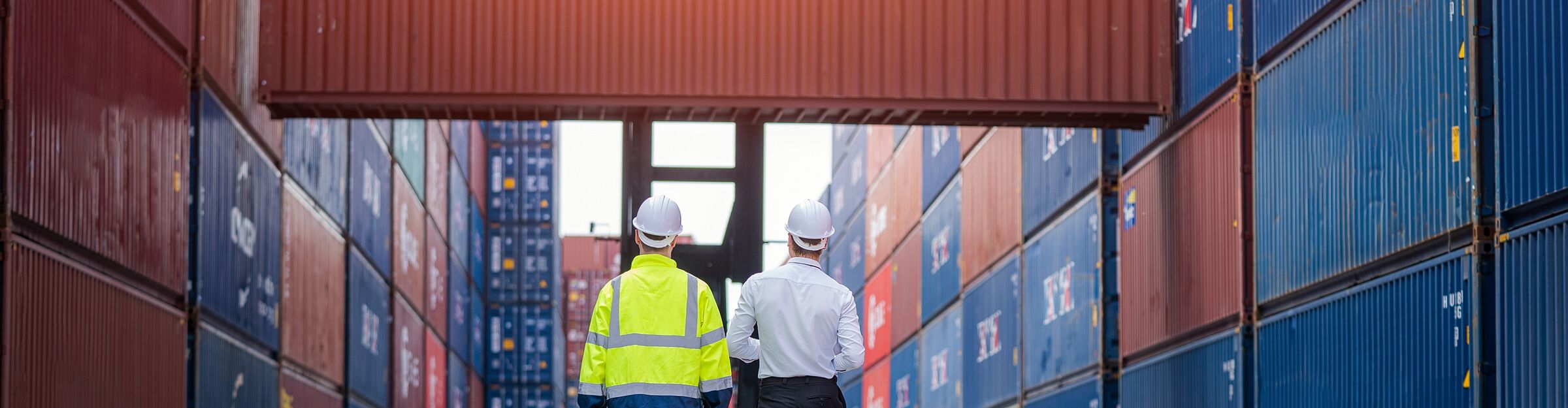 Zwei Fachkräfte mit Schutzhelm inspizieren gestapelte Container bei Off-Hire-Check im Depot.
