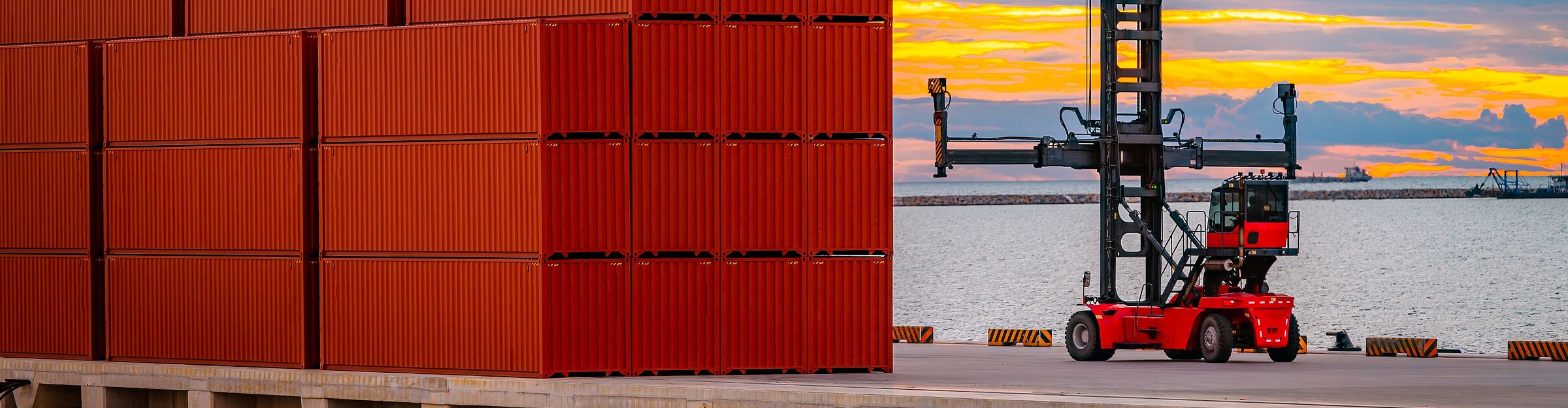 Containerstapler am Hafen bewegt rote Frachtcontainer bei Sonnenuntergang.