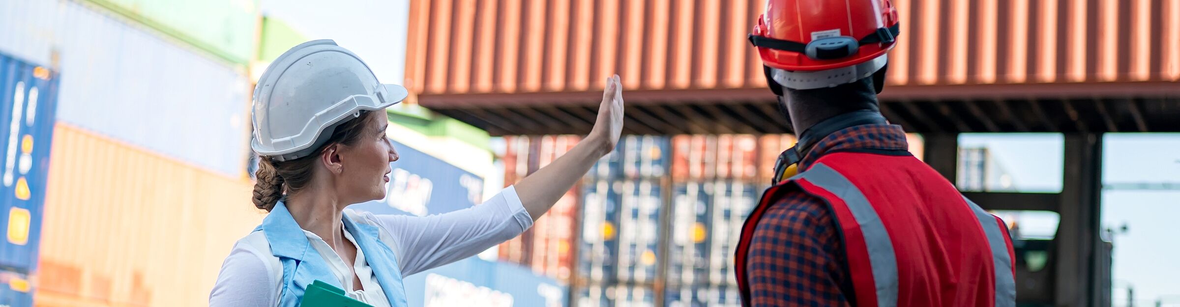 Zwei Logistikfachkräfte mit Schutzhelmen besprechen Containerbewegung auf dem Umschlagplatz.